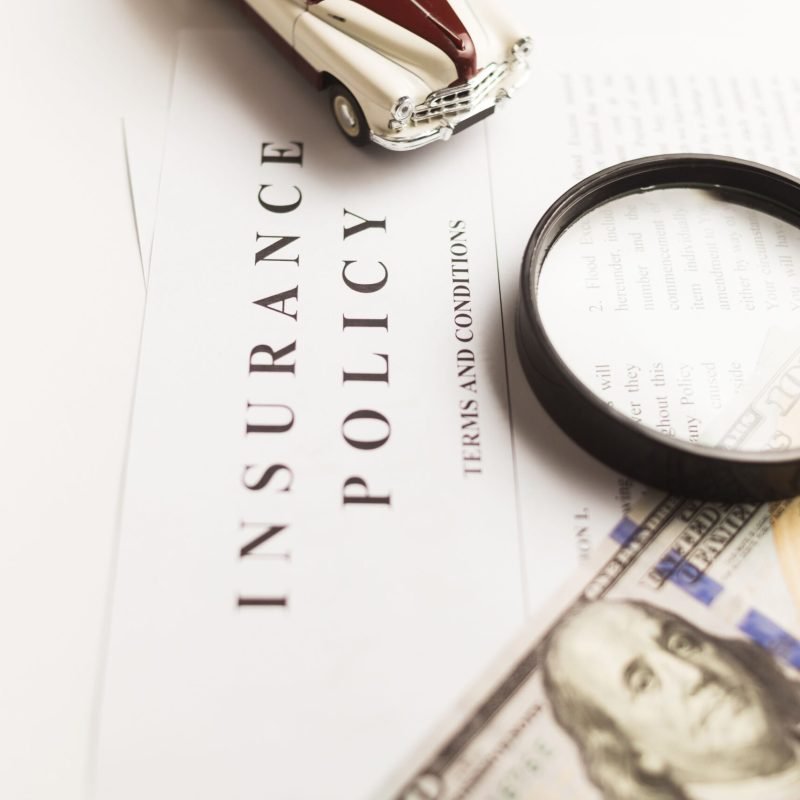 Close-up image of an insurance policy with a magnifying glass, money, and toy car.